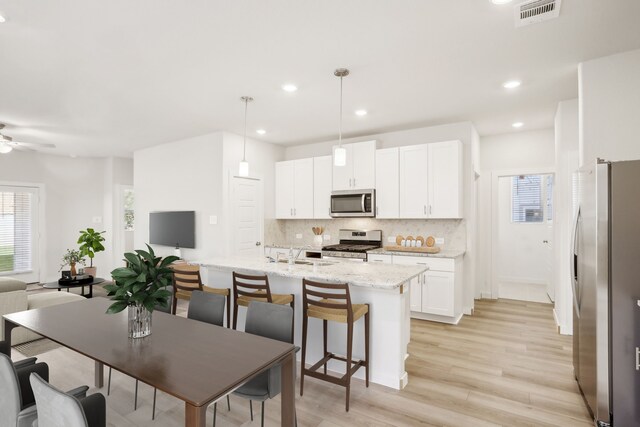 kitchen with hanging light fixtures, appliances with stainless steel finishes, backsplash, white cabinets, and a kitchen island with sink