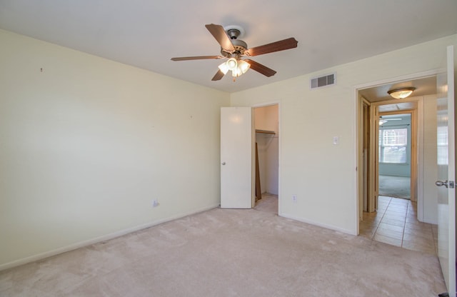 unfurnished bedroom featuring a closet, ceiling fan, a spacious closet, and light carpet