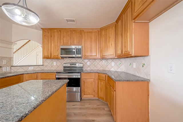 kitchen with backsplash, light wood-type flooring, appliances with stainless steel finishes, dark stone counters, and pendant lighting