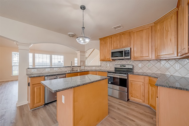 kitchen featuring light wood-type flooring, appliances with stainless steel finishes, a center island, and ornate columns