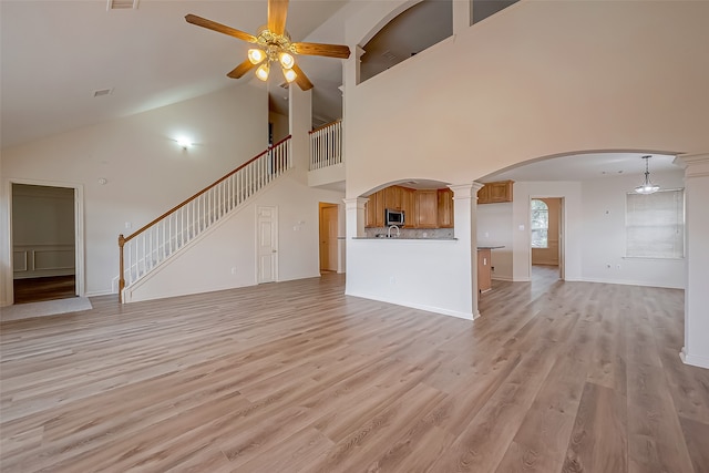 unfurnished living room featuring high vaulted ceiling, ceiling fan, light hardwood / wood-style floors, and ornate columns