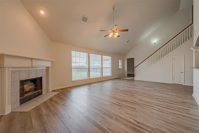 unfurnished living room with ceiling fan, a tiled fireplace, high vaulted ceiling, and light hardwood / wood-style floors