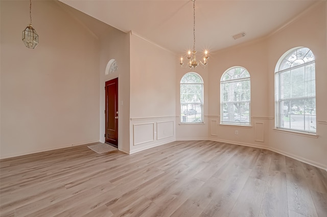 empty room featuring crown molding, a towering ceiling, light hardwood / wood-style flooring, and an inviting chandelier