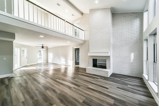 unfurnished living room featuring a fireplace, high vaulted ceiling, dark hardwood / wood-style flooring, ceiling fan, and brick wall