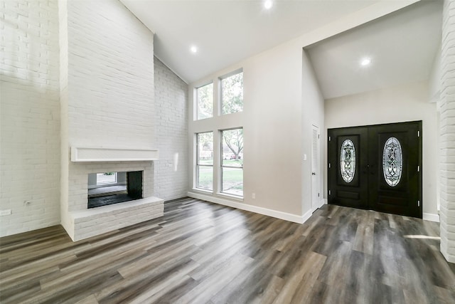 foyer entrance featuring hardwood / wood-style floors, high vaulted ceiling, a fireplace, and a healthy amount of sunlight