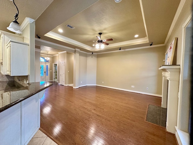 unfurnished living room featuring a tray ceiling, ceiling fan with notable chandelier, light hardwood / wood-style flooring, and ornamental molding