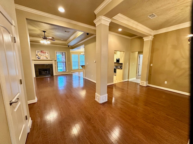 unfurnished living room with ornamental molding, ceiling fan, dark hardwood / wood-style floors, a tray ceiling, and ornate columns