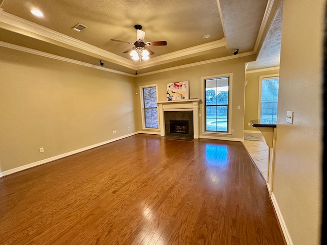 unfurnished living room featuring a high end fireplace, a textured ceiling, ceiling fan, a raised ceiling, and hardwood / wood-style flooring