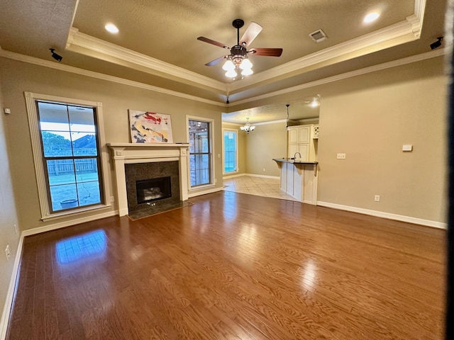 unfurnished living room with light hardwood / wood-style floors, ceiling fan with notable chandelier, and a raised ceiling