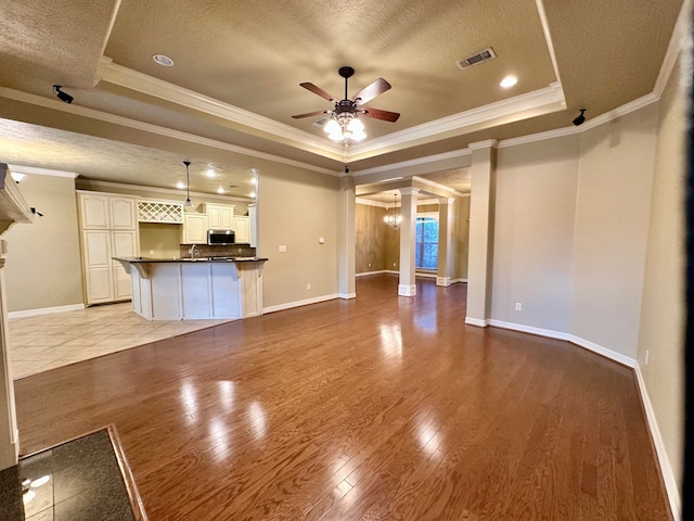 unfurnished living room featuring light hardwood / wood-style flooring, ornate columns, a tray ceiling, ceiling fan, and a textured ceiling