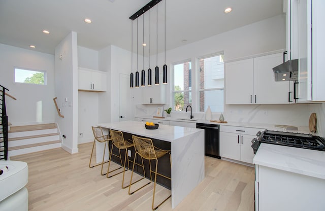 kitchen with black dishwasher, a healthy amount of sunlight, a kitchen island, and light stone countertops