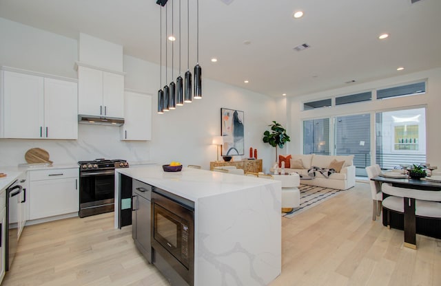 kitchen with light stone countertops, a center island, stainless steel appliances, light wood-type flooring, and white cabinets