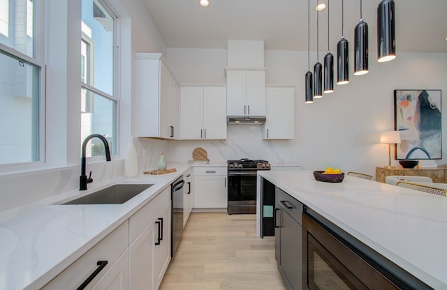 kitchen featuring light stone countertops, stainless steel appliances, white cabinetry, sink, and pendant lighting