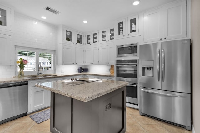 kitchen with stainless steel appliances, a kitchen island, white cabinets, and glass insert cabinets