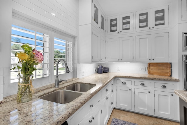 kitchen with light stone counters, white cabinetry, sink, and light tile patterned floors