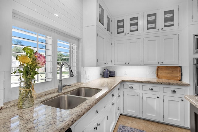 kitchen featuring light stone countertops, white cabinets, a sink, decorative backsplash, and glass insert cabinets