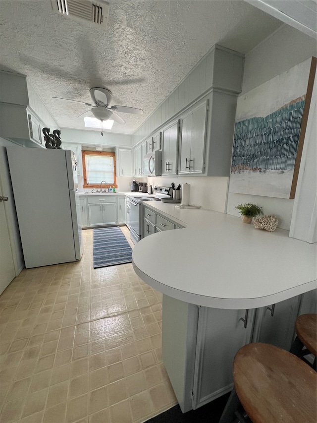 kitchen featuring white refrigerator, sink, kitchen peninsula, range with electric cooktop, and ceiling fan