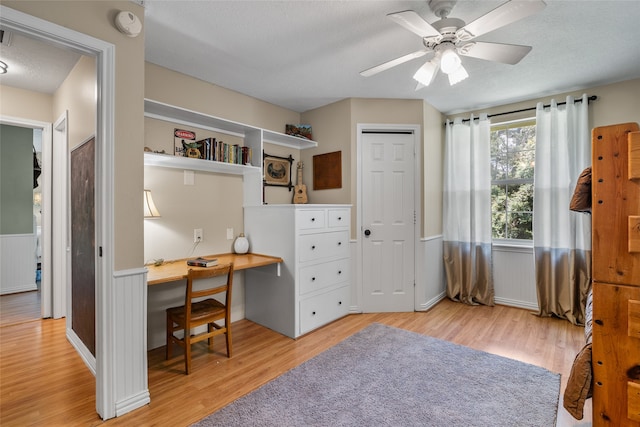 office area with a textured ceiling, built in desk, ceiling fan, and light hardwood / wood-style floors