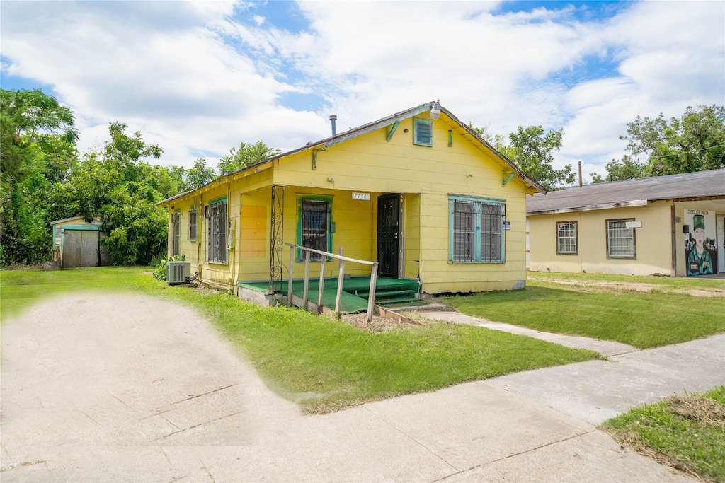 view of front of home with central AC, a front yard, and a storage shed