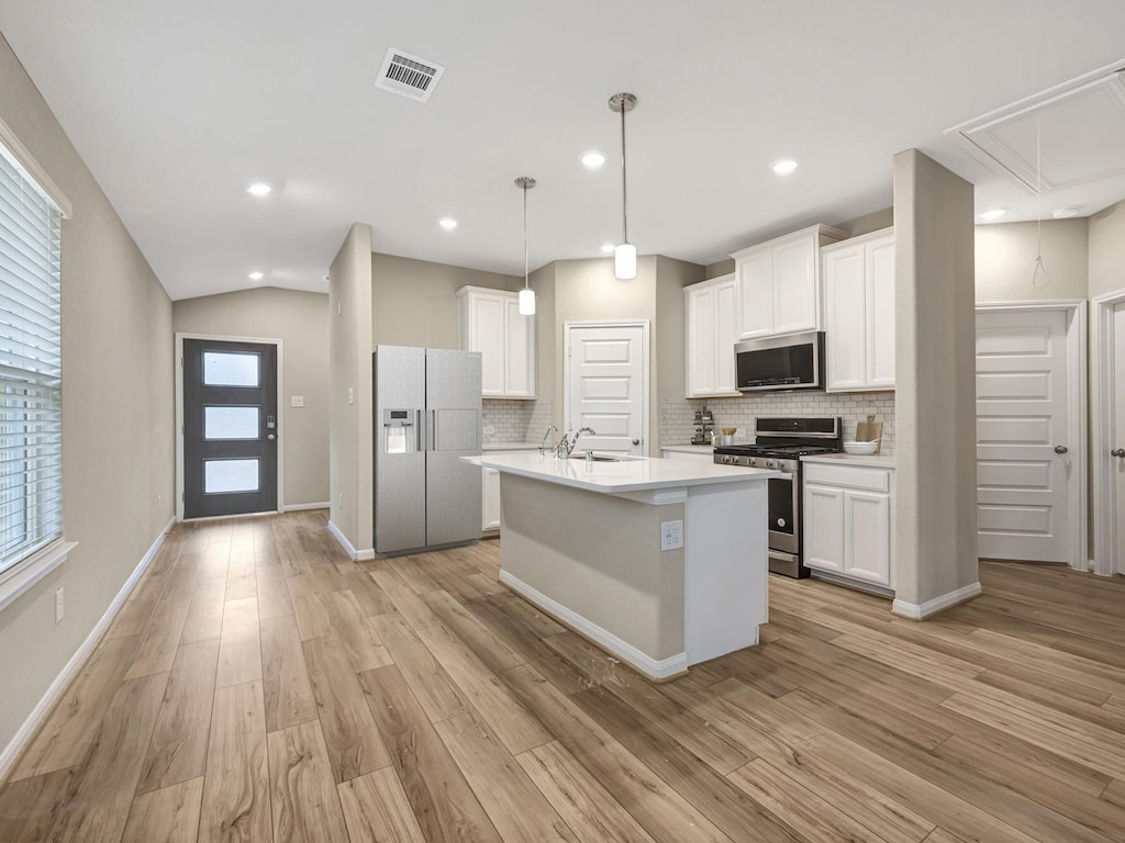 kitchen featuring white cabinets, light wood-type flooring, pendant lighting, stainless steel appliances, and a center island with sink