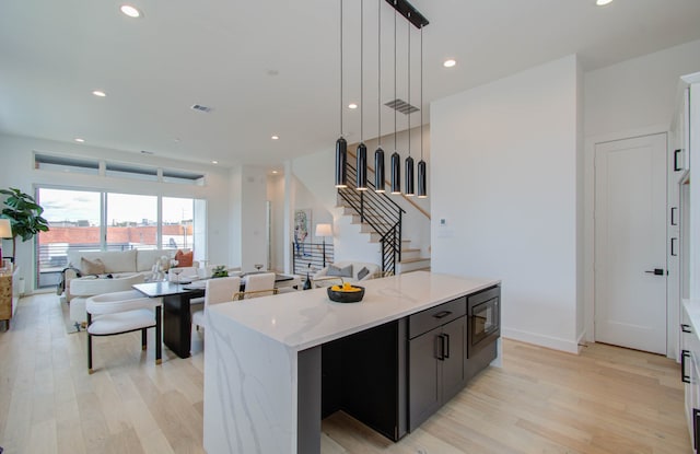 kitchen featuring light stone countertops, a center island, black microwave, pendant lighting, and light hardwood / wood-style floors