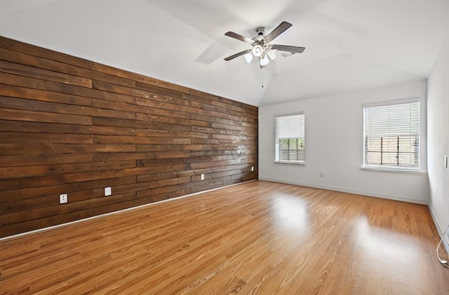 spare room with ceiling fan, light wood-type flooring, wooden walls, and lofted ceiling