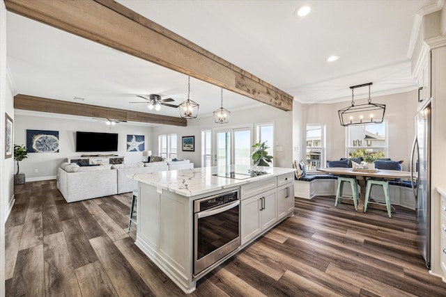 kitchen featuring pendant lighting, a center island with sink, white cabinetry, stainless steel appliances, and ceiling fan with notable chandelier