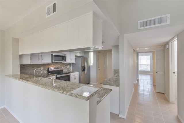 kitchen with appliances with stainless steel finishes, kitchen peninsula, sink, light stone counters, and light tile patterned flooring