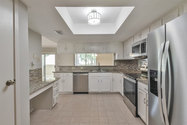 kitchen with a tray ceiling, appliances with stainless steel finishes, white cabinetry, and sink