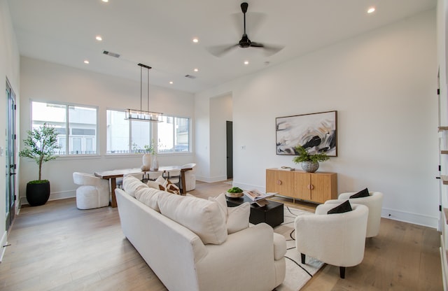 living room with ceiling fan with notable chandelier and light hardwood / wood-style flooring