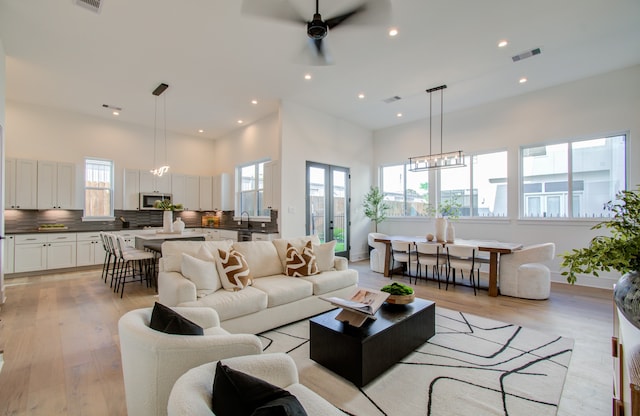 living room with a high ceiling, sink, ceiling fan with notable chandelier, and light hardwood / wood-style floors