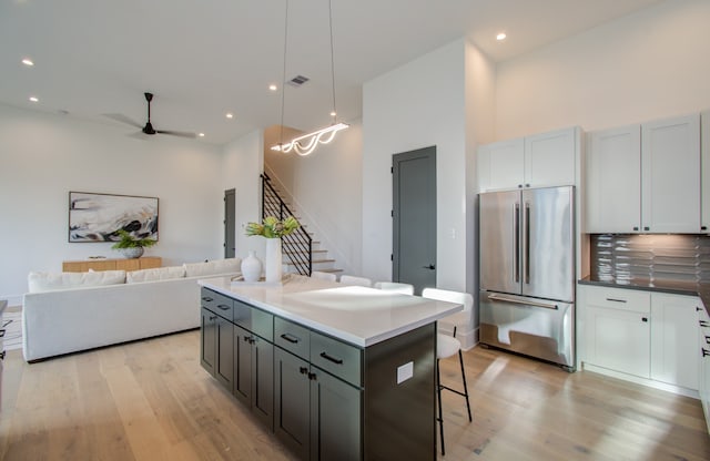 kitchen with light wood-type flooring, white cabinetry, high end fridge, ceiling fan, and a kitchen island