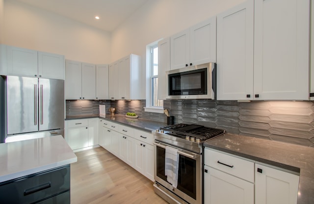 kitchen featuring light wood-type flooring, tasteful backsplash, white cabinetry, and high quality appliances