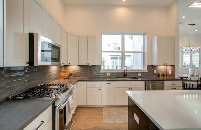 kitchen featuring white cabinetry, light hardwood / wood-style flooring, decorative light fixtures, stainless steel appliances, and sink