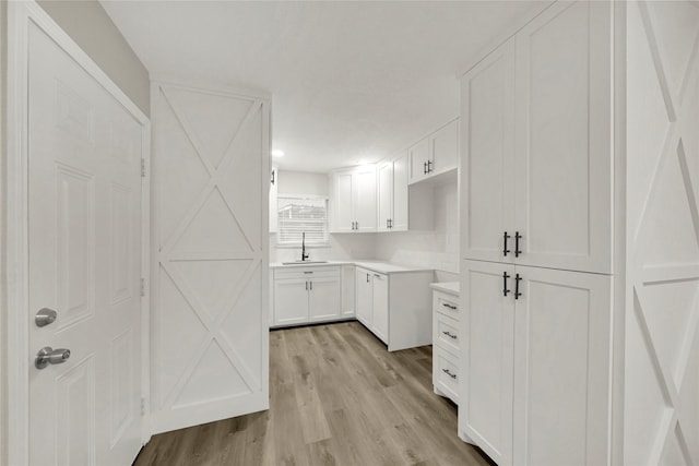 kitchen featuring white cabinetry, light countertops, light wood-type flooring, and a sink