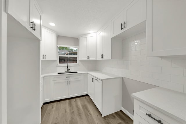 kitchen featuring tasteful backsplash, light wood-type flooring, light countertops, white cabinetry, and a sink
