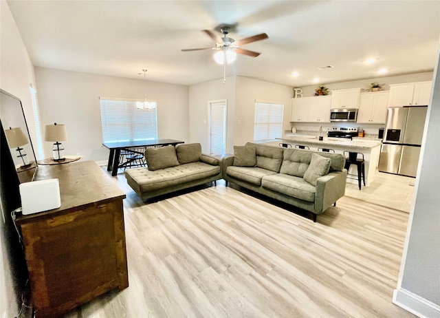 living room with ceiling fan with notable chandelier, light wood-type flooring, a healthy amount of sunlight, and sink