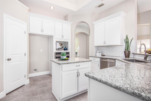 kitchen featuring appliances with stainless steel finishes, light stone counters, a center island, and white cabinetry