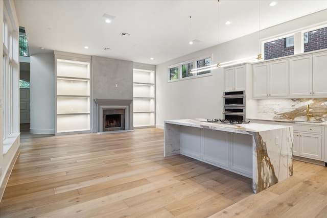 kitchen with light stone countertops, light hardwood / wood-style floors, white cabinets, a kitchen island, and stainless steel double oven