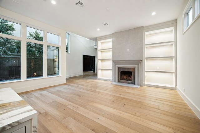 unfurnished living room featuring built in features and light hardwood / wood-style floors