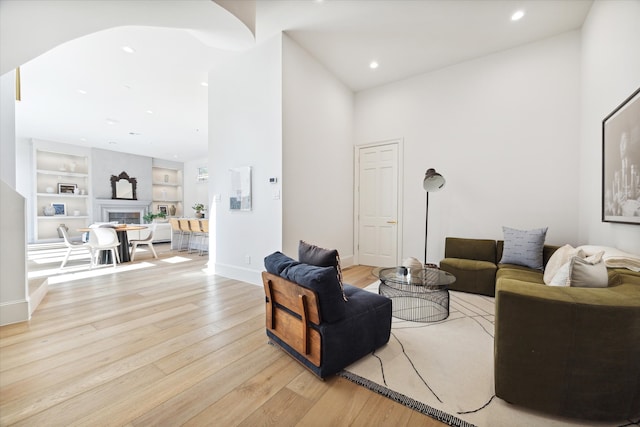 living room with built in shelves, a high ceiling, and light wood-type flooring