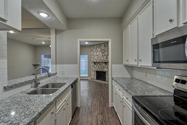 kitchen with sink, tasteful backsplash, a stone fireplace, white cabinets, and appliances with stainless steel finishes