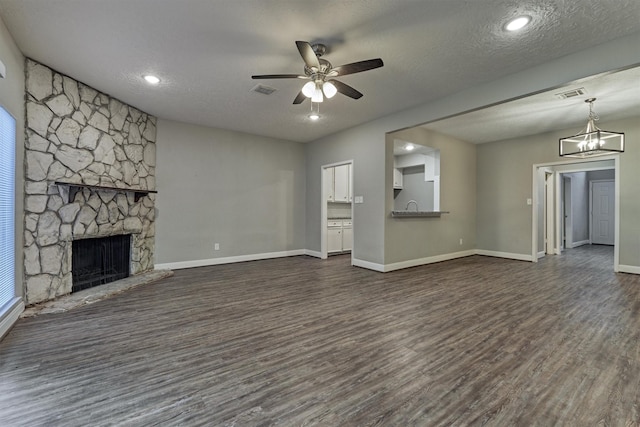 unfurnished living room featuring dark hardwood / wood-style flooring, a fireplace, ceiling fan with notable chandelier, and a textured ceiling