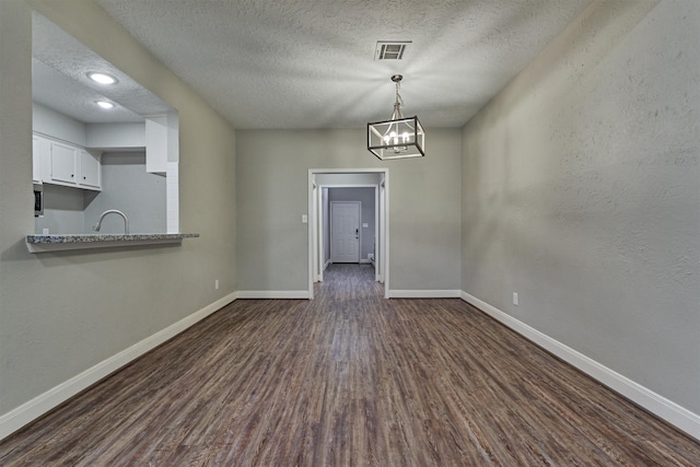 unfurnished dining area with a chandelier, a textured ceiling, and dark wood-type flooring