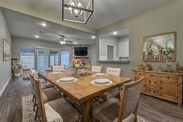 dining space featuring ceiling fan with notable chandelier, a stone fireplace, dark hardwood / wood-style flooring, and a textured ceiling