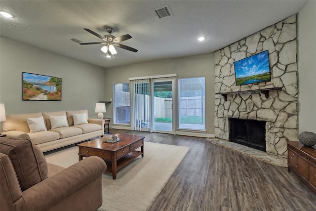 living room featuring a stone fireplace, ceiling fan, wood-type flooring, and a textured ceiling