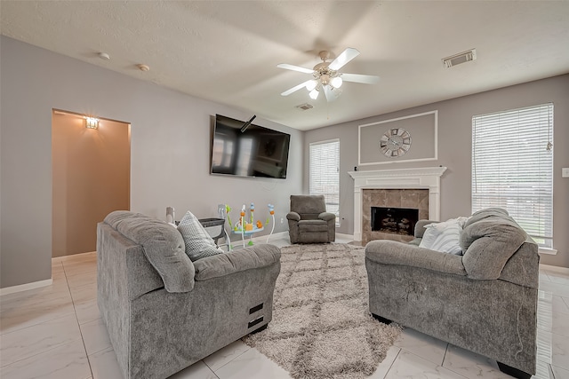 living room with a wealth of natural light, a textured ceiling, a tiled fireplace, and ceiling fan