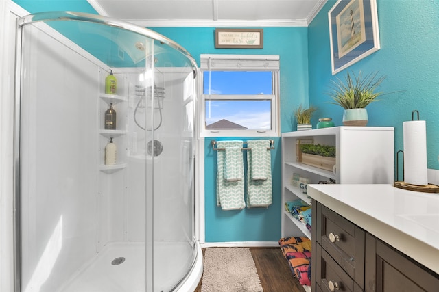 bathroom with a shower with shower door, hardwood / wood-style floors, crown molding, and vanity