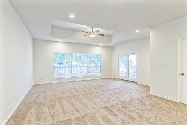 unfurnished room featuring ceiling fan, light carpet, and a tray ceiling