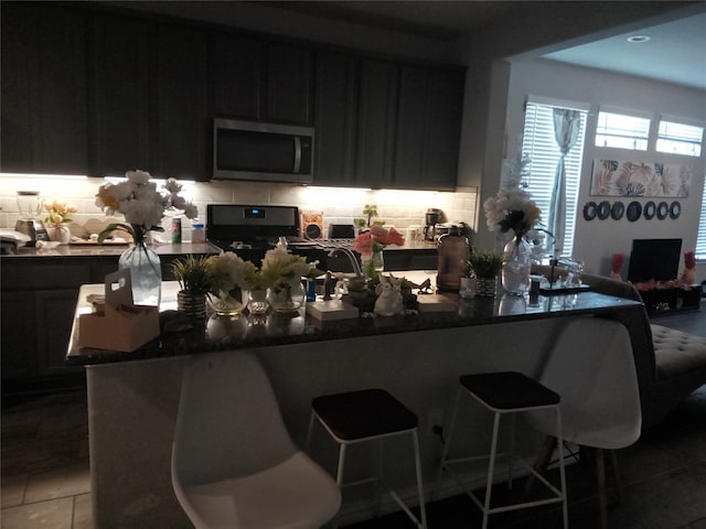 kitchen featuring a kitchen bar, stove, tasteful backsplash, and tile patterned flooring